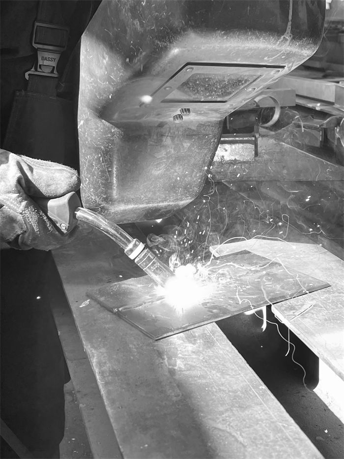 Schwarz-Weiß-Nahaufnahme: Schweißbrenner an einem Metallteil, Funken sprühen